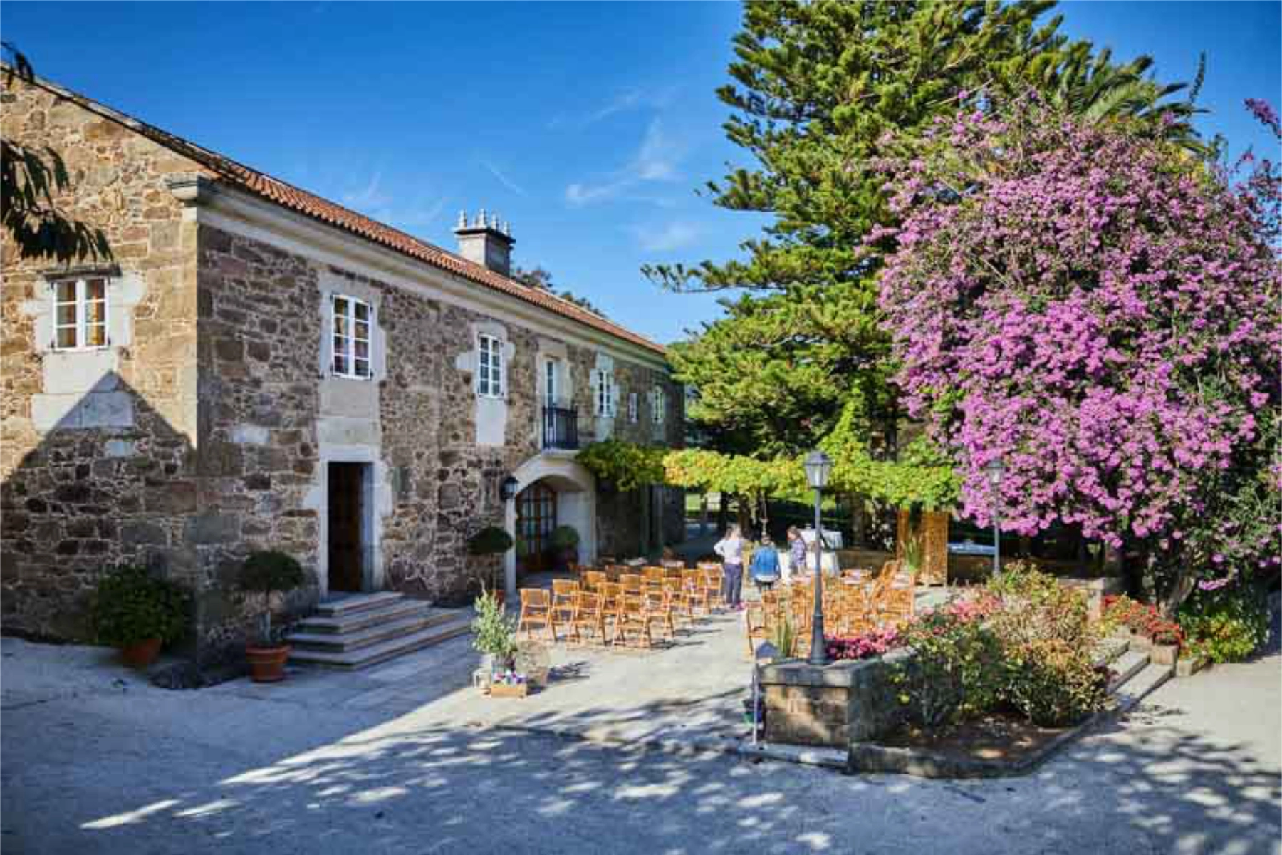 Pazo Montesclaros Fachada de piedra del Pazo Montesclaros con jardín frontal y crucero gallego, ideal para bodas con encanto rural en A Coruña